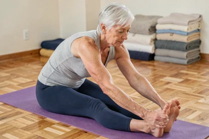 Femme de 68 ans pratiquant un étirement de flexion avant assise sur un tapis de yoga dans un centre communautaire, illustrant les exercices adaptés pour préserver la mobilité après 65 ans